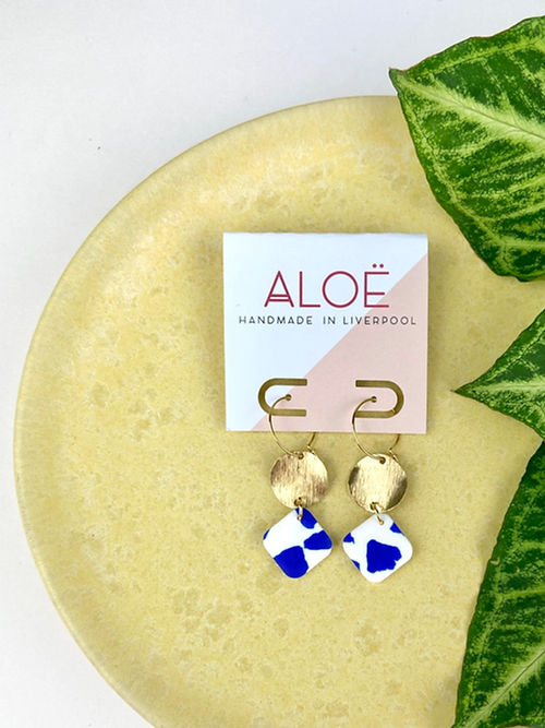 24k Gold Plated Blue & White Terrazzo Drop Hoops featuring delicate wire hoops with wavy gold disc and blue-white speckled terrazzo polymer clay diamond drops, displayed on an Aloë branded card against a pale yellow surface with green leaf accent - by Aloë Earrings | Jewellery, Gifts under £20, Earrings, Face, Aloe Earrings