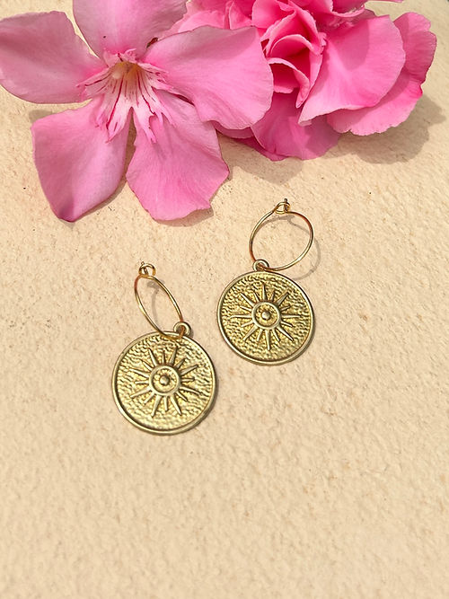 24k Gold Plated Brass Coin Mini Hoops featuring sun-embossed medallions displayed on beige background with pink oleander flowers. Delicate 15mm hoops with 21mm decorative brass coins. By Aloe Earrings - Jewellery, Gifts Under £15, Gifts under £20, Earrings, Face, Aloe Earrings