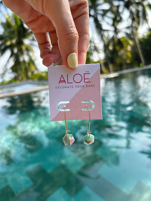 24k Gold Plated Mini Hex Oval Hoop Earrings displayed on pink Aloe branded card against tropical pool background, featuring delicate 30mm oval hoops with 10mm marbled green and purple hexagon charms. By Aloe Earrings - Jewellery, Gifts Under £15, Gifts under £20, Earrings, Face, Aloe Earrings