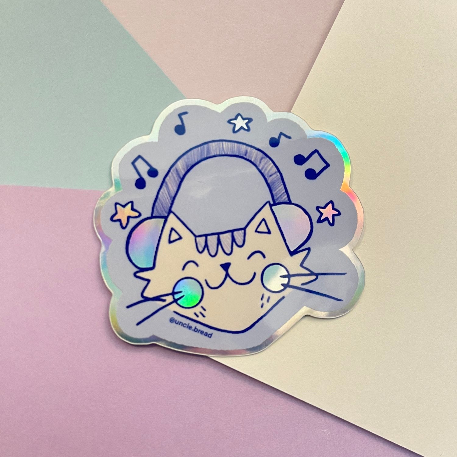 Cute cartoon cat wearing headphones surrounded by music notes and stars on a holographic cloud-shaped vinyl sticker. 'Holo Music' Cat design features a happy feline enjoying music. From Uncle Bread's Art Club Stickers Face collection.